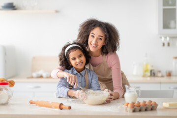 Obraz na płótnie Canvas Positive black woman and daughter kneading dough in modern kitchen