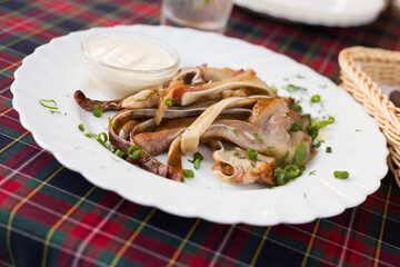 delicious smoked pork ears served with sour cream and herbs on a white plate in a restaurant