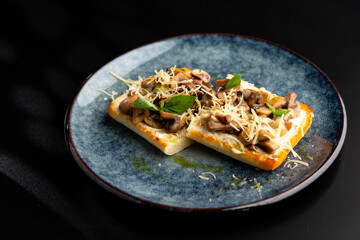 Bruschetta with mushrooms and tomatoes on a blue plate, on a black background.