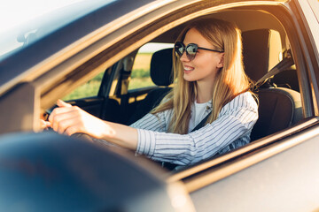 young happy smiling woman driving her new car at sunset