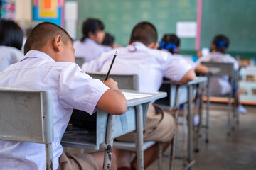 Close up of Writing test in exam with behind child asian students group concentrate in primary school, final examination desk at classroom with Thai student uniform, Education evaluation concept