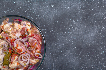 Pork ribs, sliced and marinated with onions. Shish Kebab meat in a glass bowl and spices on a textured background.Selective focus, close-up, top view.Homemade food.