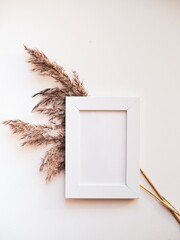 White frame mock up and dried natural pampas grass. Interior decoration element. Flatlay top view. Background boho. Minimalism design. Place for text. Selective focuson
