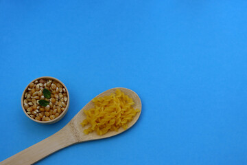 Yellow fusilli pasta in a wooden spoon and corn grains in a round bowl on a blue background. Fusilli pasta made from cornmeal.