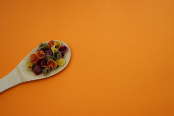 Multi-colored pasta margarita in a wooden spoon on an orange background.