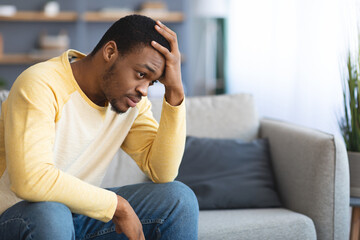 Frustrated young black man sitting on couch in living room