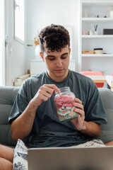 Young man using laptop and eating sweets