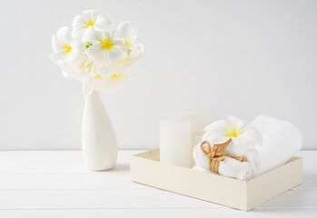 Spa composition beautiful plumeria flowers,white candles  and towels on wooden tray onver white wood table room interior background