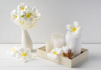 Fototapeta na wymiar Spa composition beautiful plumeria flowers,white candles and towels on wooden tray onver white wood table room interior background