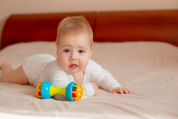 baby boy lies on his stomach with a toy on the bed in the bedroom