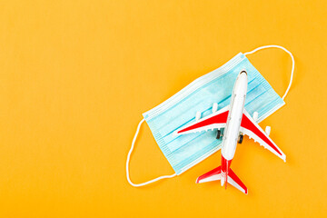 Airplane model with red wings with a blue medical mask. online ticketing and tourism concept during covid pandemic