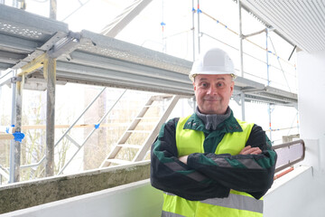 Fototapeta na wymiar senior male builder foreman, worker in white hardhat, in work clothes stands on a construction site, the concept of repair of buildings, structures, scaffolding