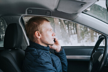 Young caucasian male blond driver is sitting in the car and talking on a smartphone. Close-up portrait. Travel concept.