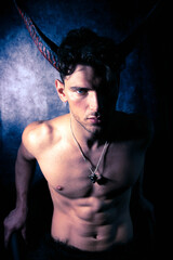 Sexy shirtless male devil with horns and muscular body showing pecs and abs looking at camera