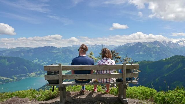 Young couple sitting on bench on top of a mountain relaxing and enjoying the scenery of Zell am Zee panorama in Austria