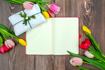 Multicolored tulips, notebook for mock up on a wooden surface. Floral background with copy space