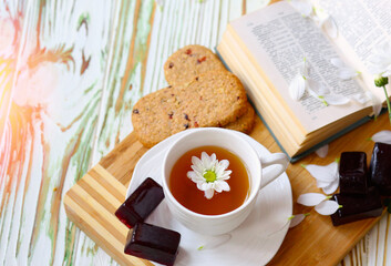 Flat lay chamomile tea in a white cup on a saucer where a wooden substrate and decor are book and flowers. Sweets. Marmalade. Morning concept