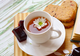 Flat lay, а cup on a platter of fragrant herbal tea with natural healthy sweets. Coarse wheat marmalade and cookies. Top view, wood substrate decorated with flowers and petals. Healthy food concept