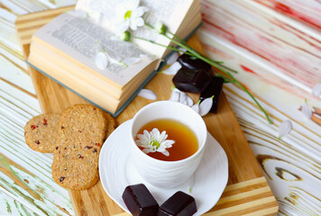 Flat lay chamomile tea in a white cup on a saucer where a wooden substrate and decor are book and...