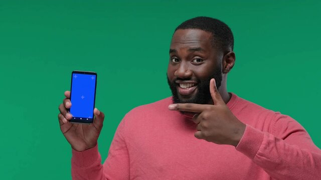 Happy young black MAN showing his phone screen with chroma key and pointing to it on Green Screen, Chroma