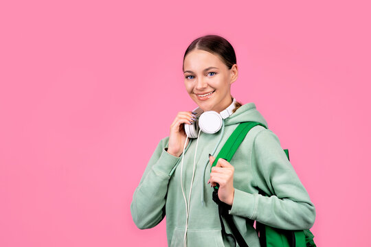 Happy smiling woman, student girl goes to study with a backpack and with headphones. Portrait on a solid monochrome pink background.