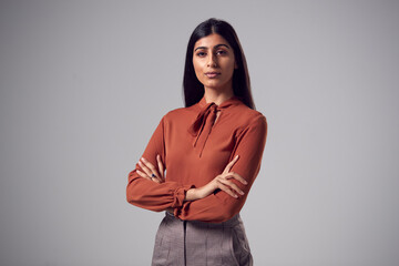 Studio Portrait Of Serious Young Businesswoman With Folded Arms Against Plain Background