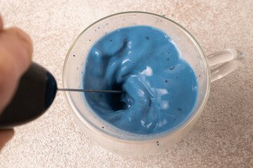 Hand mixer for beating the blue matcha latte. Preparing blue matcha latte in a glass mug. Whisking matcha tea