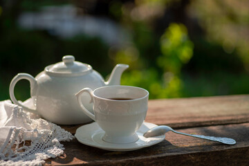 Elegant cup, lace tablecloth, teapot, wooden table. Outdoor breakfast, picnic, brunch, spring mood. Soft focus