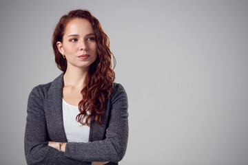 Studio Portrait Of Serious Young Businesswoman With Folded Arms Against Plain Background