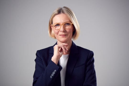 Studio Portrait Of Smiling Mature Businesswoman Wearing Glasses Against Plain Background