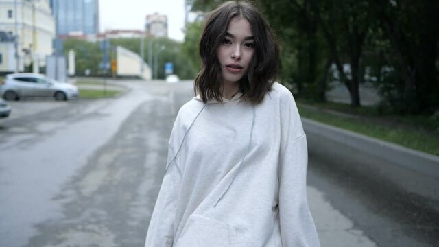 Video of a beautiful young girl of Asian appearance walks around the city and turns on camera raising her hands up. High quality FullHD footage