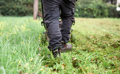 Man with lawn mower cuts the grass  in the park. Grass grows quickly during favorable season, it is periodically trimmed. Green, well-groomed, beautiful lawns delight others. Outdoors.