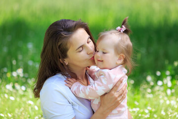 Mother and daughter play, spend time together. Mom hugs girl with love. Woman kisses baby on cheek. Parental care of child. Floral summer, spring background. Family relationship concept. Mothers day