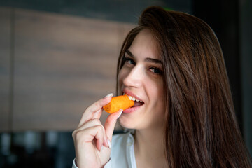 Close up woman eating nibbling carrot and smiling in the kitchen interior.. Health diet food....