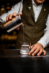 Fototapeta na wymiar bartender pours drink from steel mixing cup with strainer into glass with ice