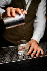 bartender carefully pours drink from steel mixing cup into old-fashioned glass
