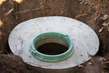 Construction of a septic tank. Large concrete rings embedded in the ground, from above an open sewer hatch, unprotected by a cover from falling