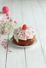 close up of small еaster cake with white icing on white plate on the side white flowers on  white table with copy space