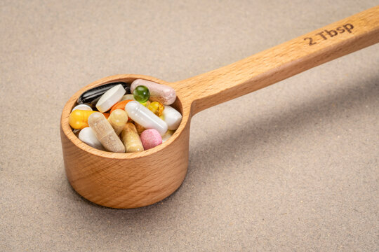 vitamins and supplement pills in wooden measuring scoop (2 tablespoons), healthy living or supplement junkie concept