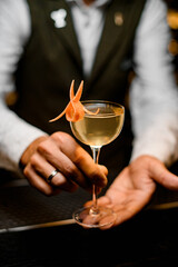 wine glass with refreshing cold drink decorated with orange zest in hands of bartender