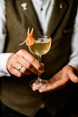 wine glass with refreshing cold drink decorated with citrus zest in hands of bartender