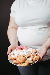 Overweight woman holding plate with tasty sweets