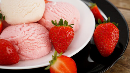 Delicious strawberry ice cream with fresh strawberrieson a white and black plate