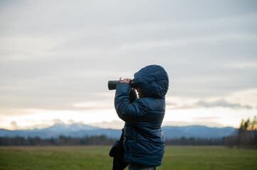 Toddler boy standing outside looking through binoculars