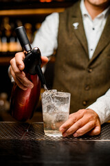 male bartender adds soda water from siphon to crystal glass with drink