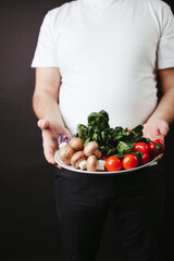 Overweight man holding plate with fresh vegetables
