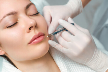 Lip augmentation and correction procedure in a cosmetology salon. The specialist makes an injection in the patient lips.