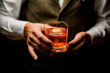 old-fashioned glass with cold alcoholic cocktail in hands of male bartender