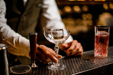 crystal wine glass with ice cube stands on bar and bartender's hand holds it