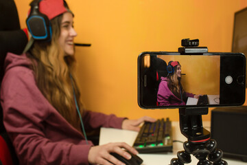 Gamer recording live for her online channel with smartphone during quarantine. Concept gamer video streaming during corona pandemic. Close up smartphone recording girl gamer playing video game.